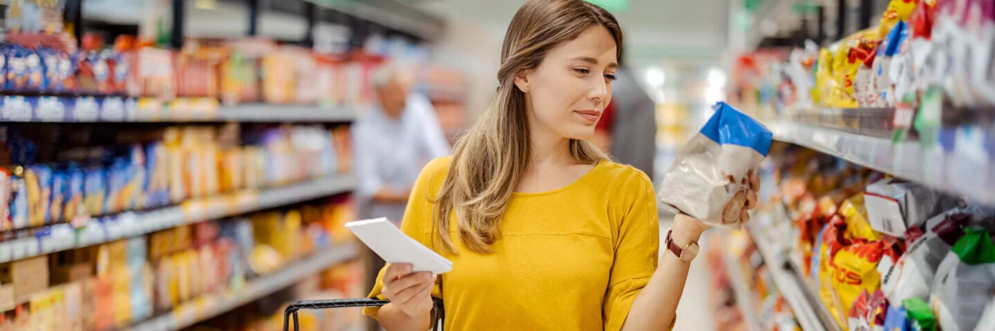 Eine junge Frau schaut sich beim Einkaufen im Supermarkt die Nährwertangaben eines Produktes an.