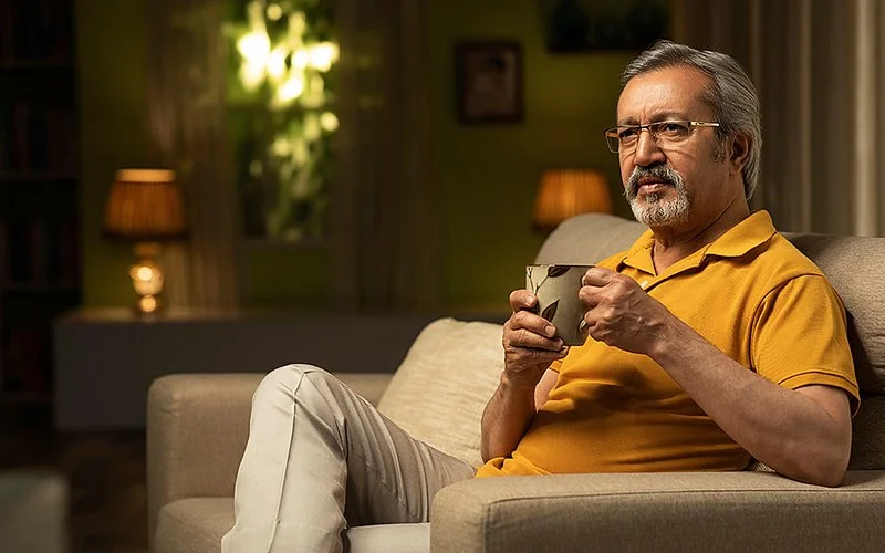 Ein älterer Mann sitzt auf der Couch und trinkt vor dem Schlafengehen einen Tee als entspannendes Ritual.