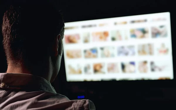 Ein Mann, der unter Sexsucht leidet, sitzt vor einem Bildschirm und schaut Pornos.