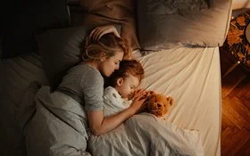 Draufsicht auf eine schlafende Frau und ein schlafendes Kind in einem Bett.