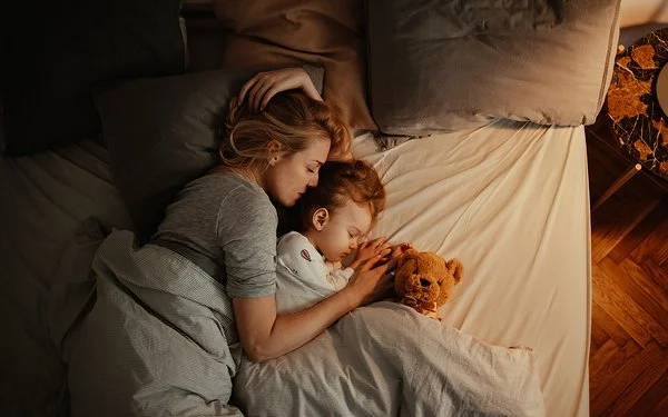 Draufsicht auf eine schlafende Frau und ein schlafendes Kind in einem Bett.