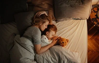 Draufsicht auf eine schlafende Frau und ein schlafendes Kind in einem Bett.