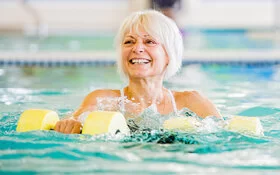 Frau trainiert mit Geräten im Wasser, damit das Schwimmen noch effektiver wird.