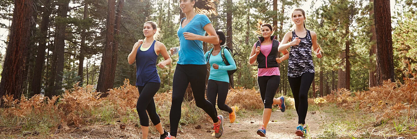 Eine Gruppe junger Frauen joggt in Sportkleidung durch einen Wald.