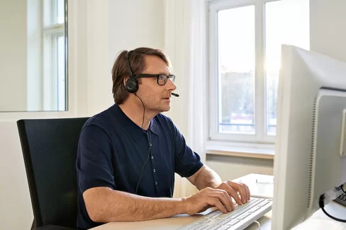 Ein Mann mit Headset sitzt vor einem Bildschirm und schreibt etwas auf das Keyboard.