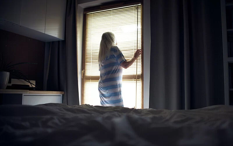 Eine Frau dunkelt ihr Schlafzimmer mit einer Jalousie ab, um es kühl zu halten.