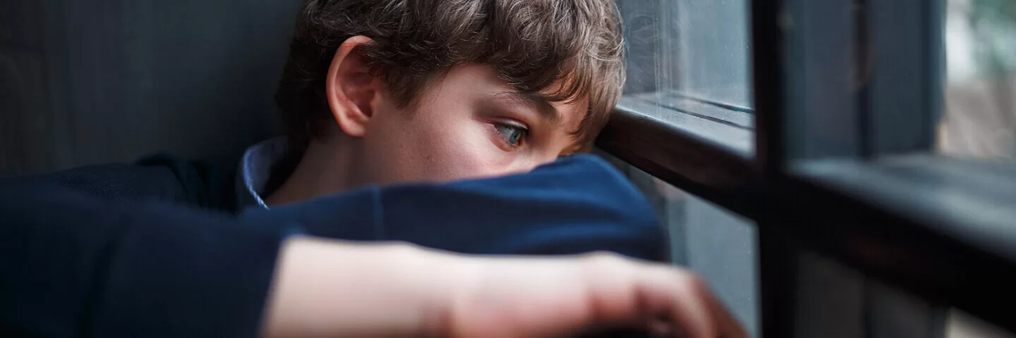 Depression: Kind mit psychischer Erkrankung guckt traurig aus dem Fenster.