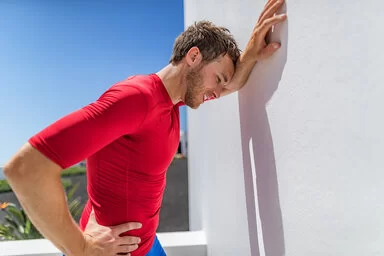 Ein junger Mann lehnt sich erschöpft nach dem Sport an eine Wand und ringt nach Atem.