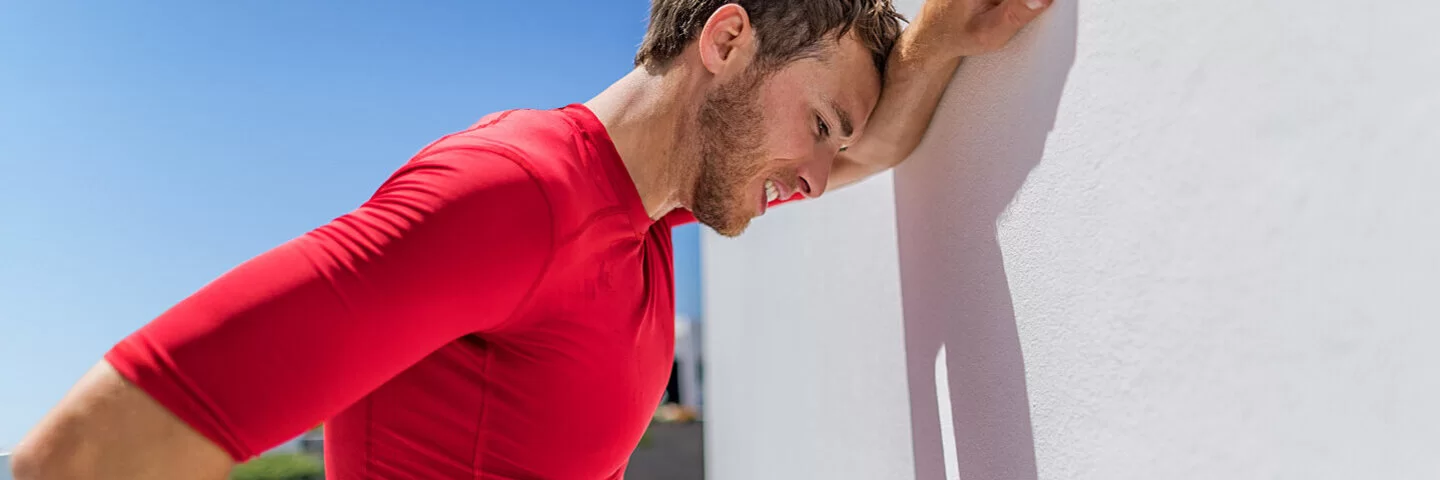 Ein junger Mann lehnt sich erschöpft nach dem Sport an eine Wand und ringt nach Atem.