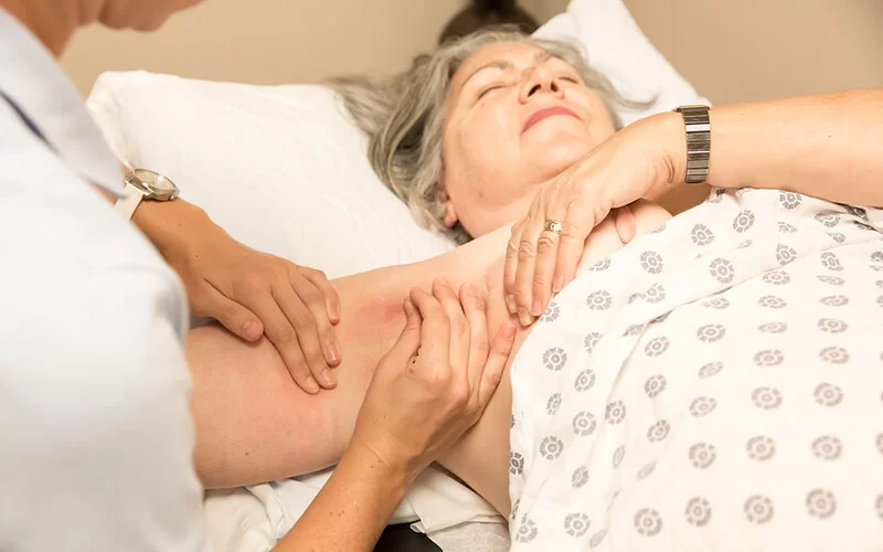 Eine Physiotherapeutin führt bei einer älteren Patientin mit Lymphödem im Oberarm eine manuelle Lymphdrainage durch.