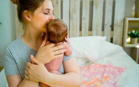 Frau hält Neugeborenes auf dem Arm, das den Nestschutz der Mutter hat.