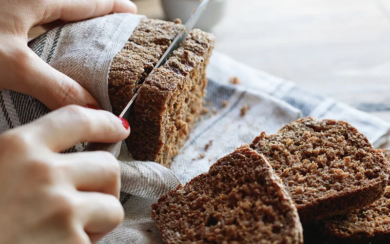 Eine Frau schneidet sich Vollkornbrot für ein gesundes Pausenbrot ab.