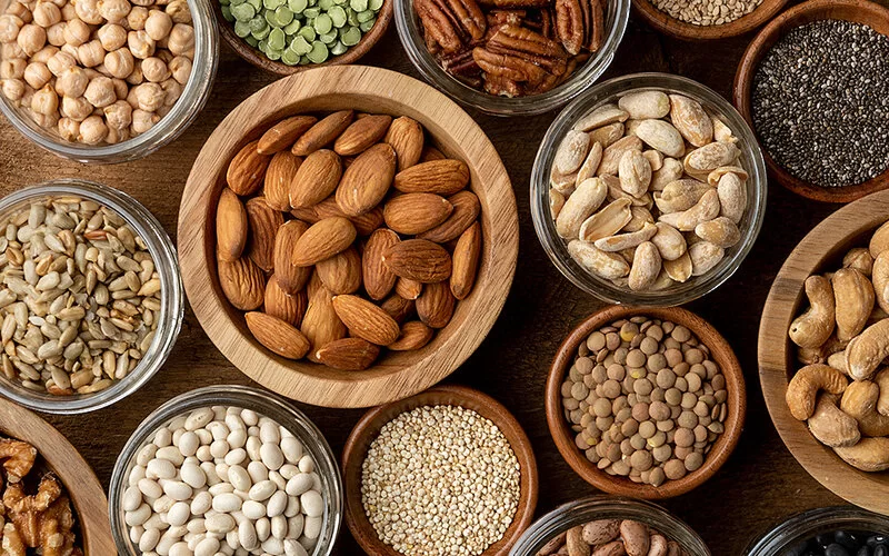 Auf einem Holztisch stehen diverse Schalen mit Nüssen, Samen und Hülsenfrüchten, die ein Bestandteil der Planetary Health Diet sind.