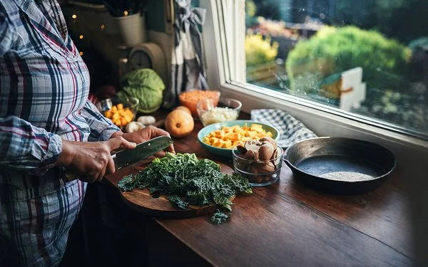 Eine Frau schneidet Grünkohl auf einem Schneidebrett in der Küche.