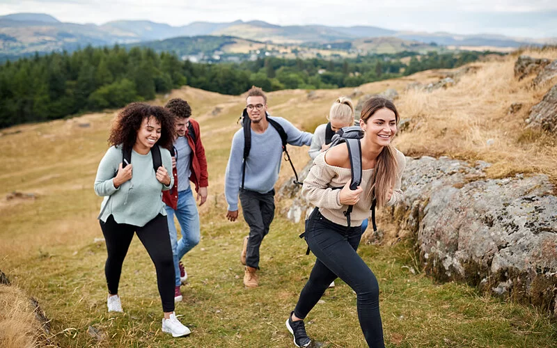 Eine Gruppe von insgesamt fünf Männern und Frauen wandern bergauf auf einer Wiese.