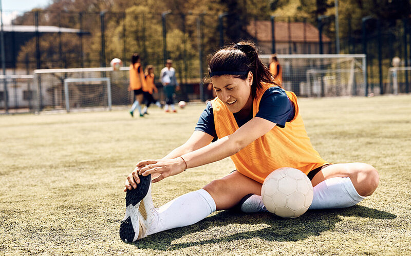 Eine Fußballerin dehnt sich auf dem Fußballplatz.