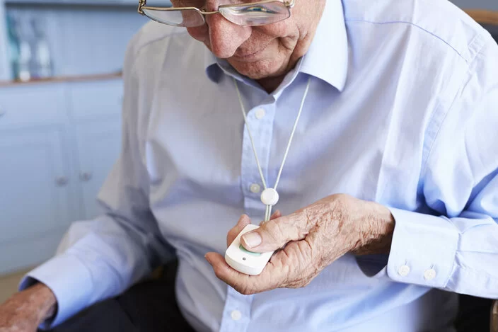 Ein älterer Herr sitzt auf einem Stuhl und betätigt einen Hausnotrufknopf.