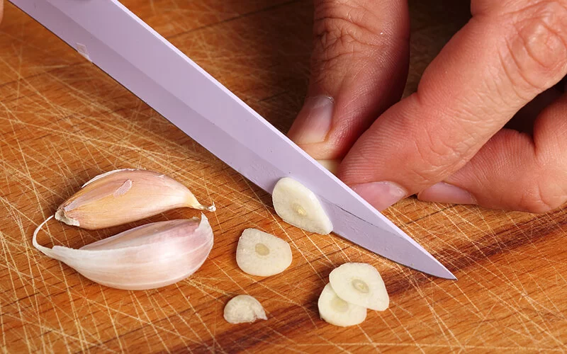 Eine Knoblauchzehe wird fein in Scheiben geschnitten.