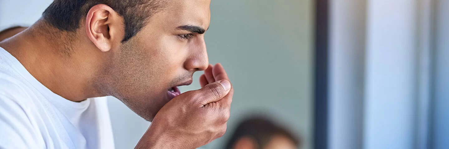 Ein Mann atmet in seine Hand um zu prüfen, ob er Mundgeruch hat.