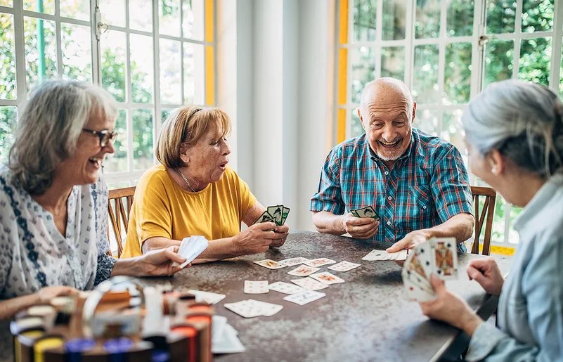 Vier Senioren und Seniorinnen spielen zusammen an einem Tisch Karten.