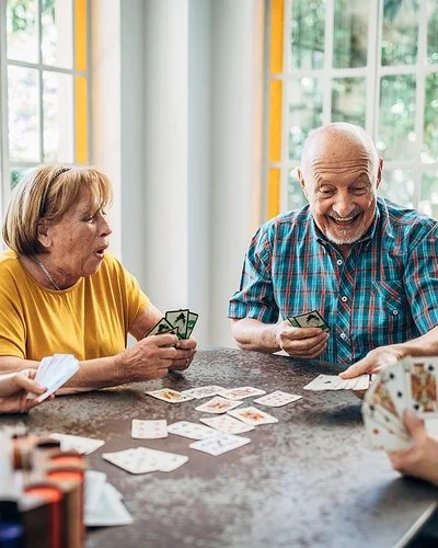 Vier Senioren und Seniorinnen spielen zusammen an einem Tisch Karten.