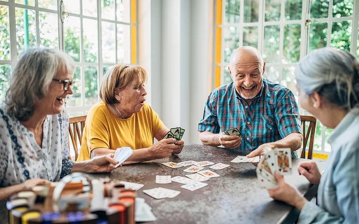 Vier Senioren und Seniorinnen spielen zusammen an einem Tisch Karten.
