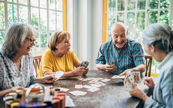 Vier Senioren und Seniorinnen spielen zusammen an einem Tisch Karten.