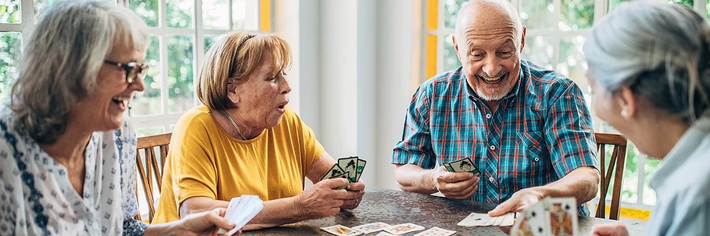 Vier Senioren und Seniorinnen spielen zusammen an einem Tisch Karten.