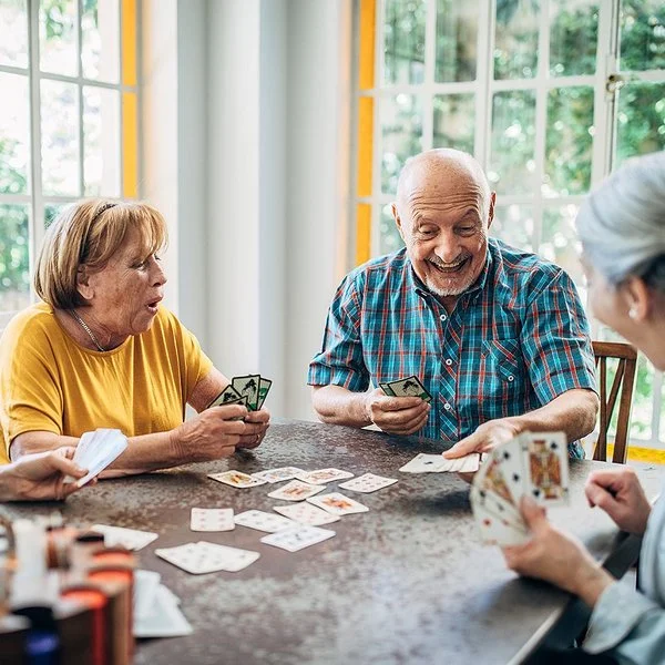 Vier Senioren und Seniorinnen spielen zusammen an einem Tisch Karten.