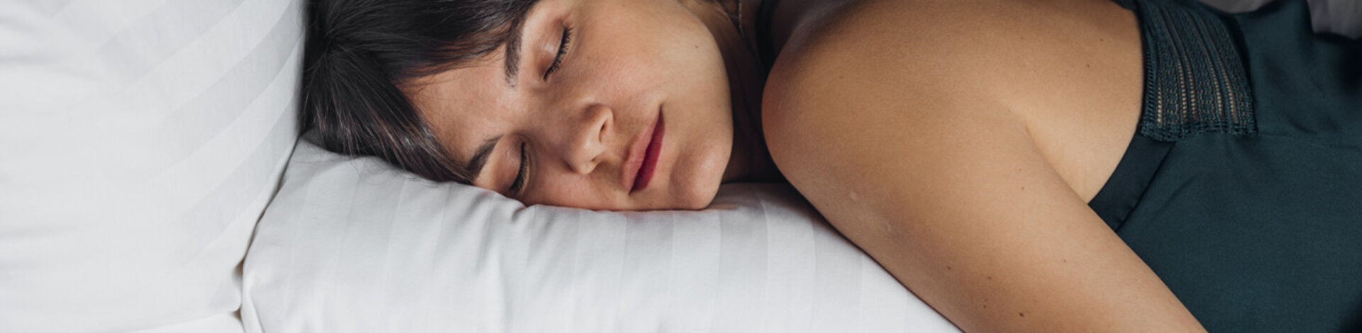 Eine junge Frau liegt in einem Bett auf einem Kopfkissen und schläft.