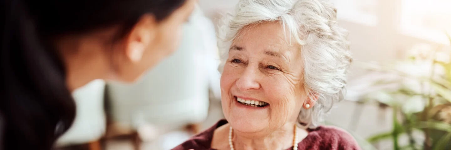Eine ältere Dame lächelt eine junge Pflegerin an.