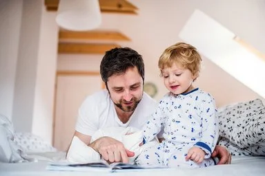 Vater liegt neben seinem Sohn, gemeinsam wird ein Buch angeschaut.
