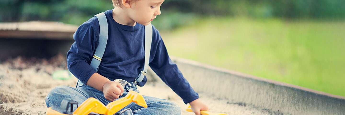Ein Kind mit Autismus spielt konzentriert im Sandkasten.