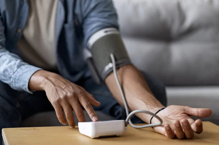 Ein Mann sitzt zuhause auf dem Sofa und verwendet ein Blutdruckmessgerät.