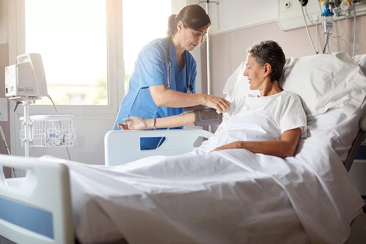 Eine Frau legt einem Mann im Krankenhausbett ein Blutdruckmessgerät an.