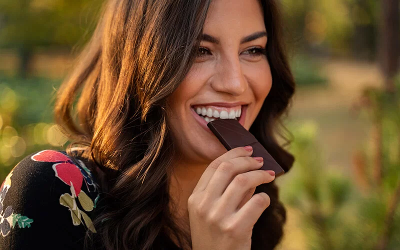 Junge Frau isst ein Stück dunkle Schokolade.