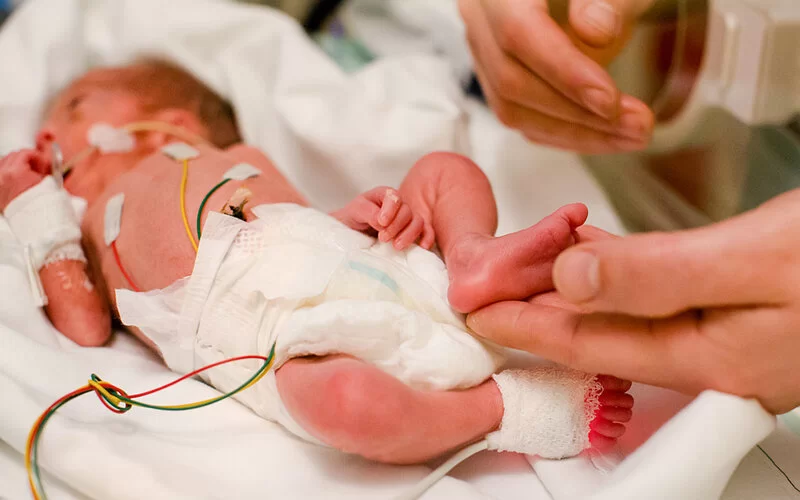 Ein Frühchen wird intensivmedizinisch betreut und jemand streichelt den Babyfuß.