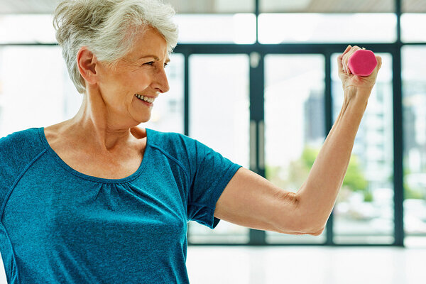 Eine Seniorin hält eine kleine Hantel in der Hand und treibt Sport, um Osteoporose vorzubeugen.
