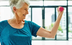 Eine Seniorin hält eine kleine Hantel in der Hand und treibt Sport, um Osteoporose vorzubeugen.