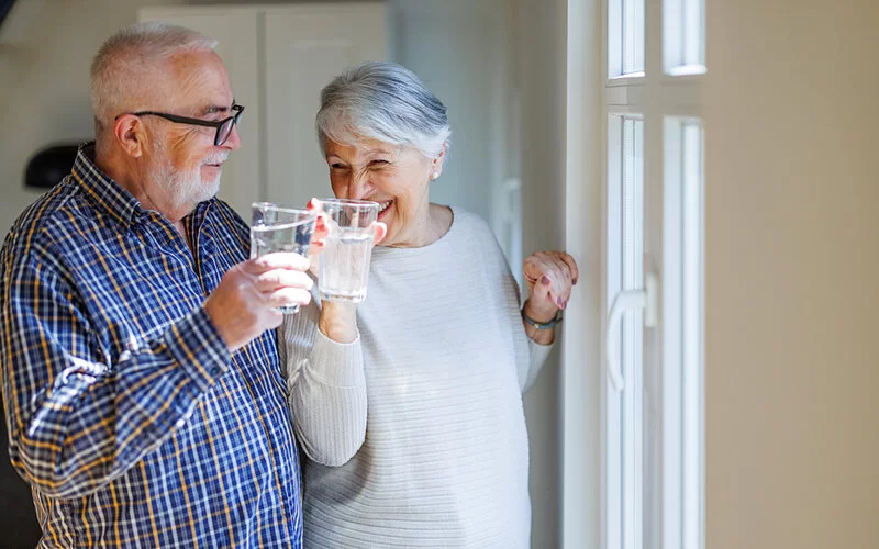 Ein älteres Paar stößt mit einem Glas Wasser an – ausreichend viel zu trinken hilft, die Verdauung anzuregen.