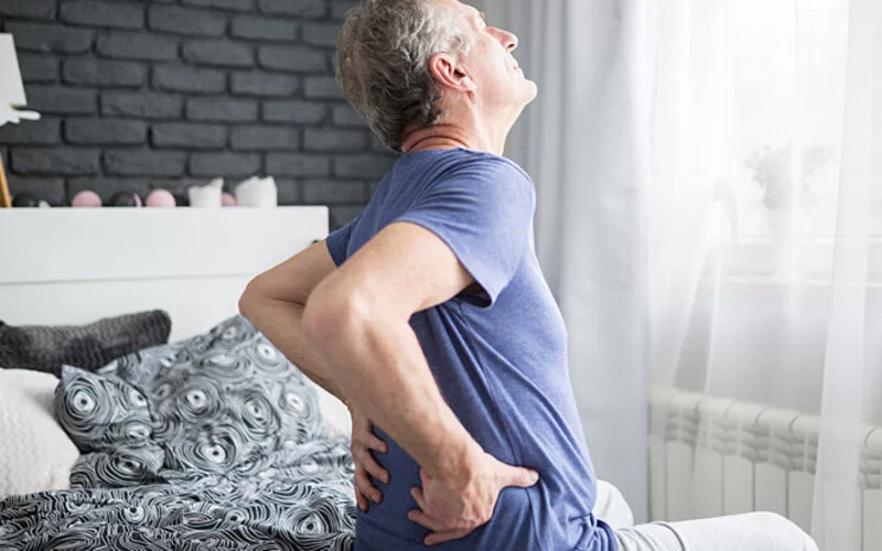 Älterer Mann wacht mit Rückenschmerzen auf, aber gehören diese zum menschlichen Alterungsprozess dazu?