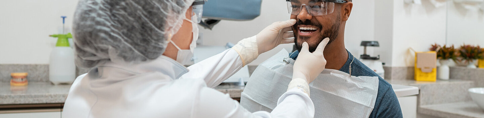 Ein Zahnarzt tastet den Kiefer eines Patienten ab. Beide tragen Schutzkleidung, um eine Infektion mit dem Coronavirus in der AOK-Zahnklinik zu verhindern.