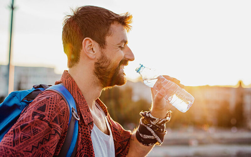 Ein Mann auf Reisen trinkt Wasser bei Hitze.