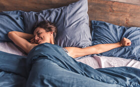 Eine Frau liegt im Bett und streckt sich.