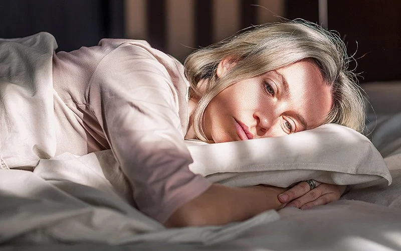Ein Frau liegt mit offenen Augen auf der Seite im Bett.