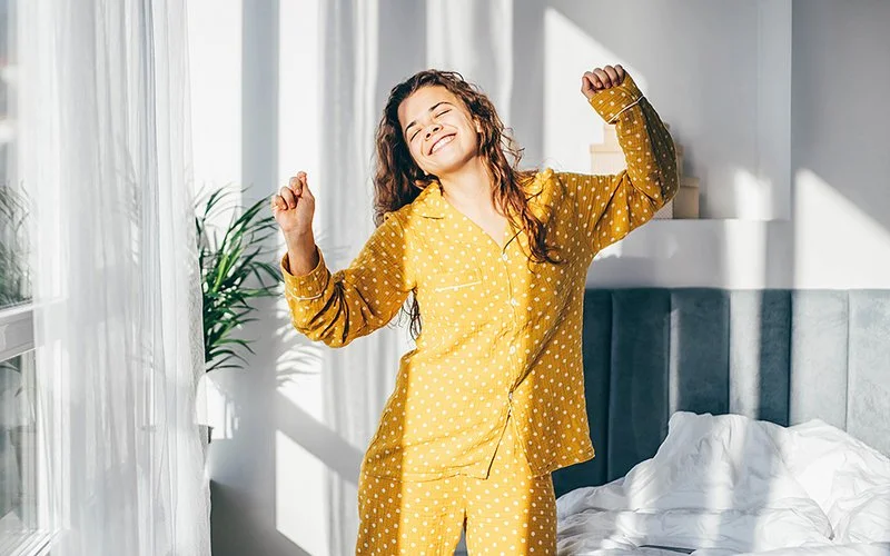 Eine Frau im gelben Pyjama tanzt in ihrem Schlafzimmer.