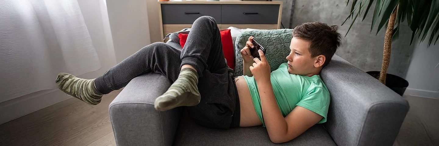 Ein Junge liegt mit einem Smartphone in der Hand auf einem Sessel.