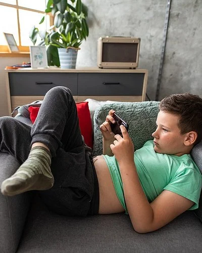 Ein Junge liegt mit einem Smartphone in der Hand auf einem Sessel.