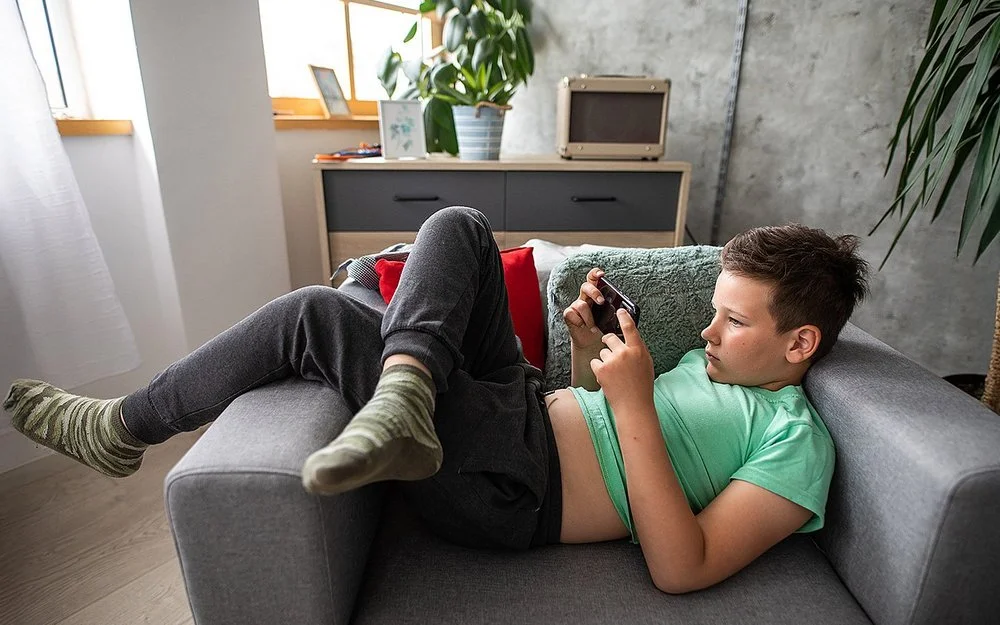 Ein Junge liegt mit einem Smartphone in der Hand auf einem Sessel.