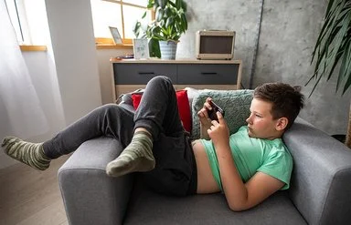 Ein Junge liegt mit einem Smartphone in der Hand auf einem Sessel.